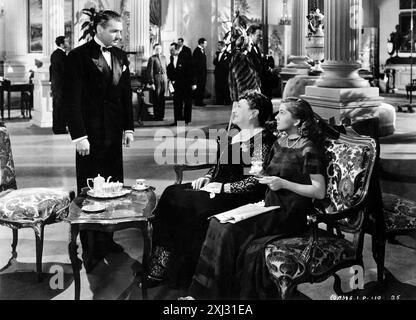 Rebecca, Alfred Hitchcock. Scène de 'Rebecca' d'Alfred Hitchcock avec Laurence Olivier et Joan Fontaine, 1940. A Monte Carlo, Max de Winter (Laurence Olivier) s’arrête pour parler à MRS Edythe Van Hopper (Florence Bates) seulement après avoir reconnu sa compagne (Joan Fontaine) Banque D'Images