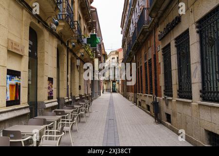 Astorga, Espagne - 4 juin 2023 : des tables vides bordent le trottoir d'une rue étroite d'Astorga, Espagne, le soleil tranquille de l'après-midi projetant de longues ombres sur le sol Banque D'Images