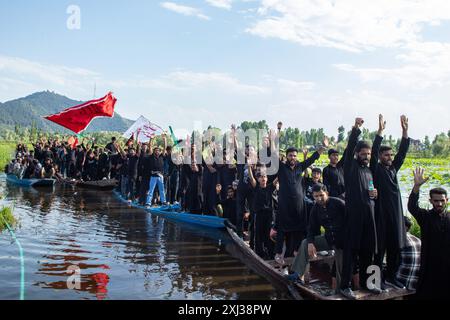 Srinagar, Inde. 16 juillet 2024. Les chiites du Cachemire en deuil hissent des drapeaux religieux en criant des slogans tout en ramant sur des bateaux pendant la procession à l'intérieur du lac Dal à Srinagar le 9 de Mouharram, le premier et le plus Saint mois du calendrier islamique. Les musulmans chiites commémorent Mouharram comme un mois de deuil en souvenir du martyre du petit-fils du prophète islamique Mahomet, Imam Hussain, qui a été tué avec les membres de sa famille à Ashura (le 10ème jour de Mouharram) dans la bataille de Karbala dans le sud de l'Irak en 680 après J.-C. crédit : SOPA images Limited/Alamy Live News Banque D'Images