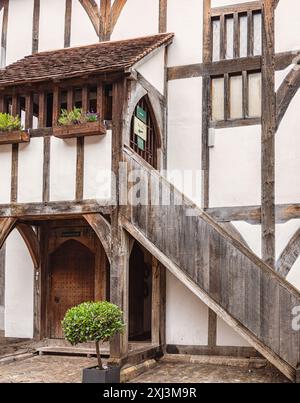 Un bâtiment historique à colombages. Une porte se trouve sous une galerie et un escalier monte sur le côté jusqu'à une grille en fer. Banque D'Images