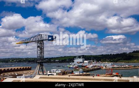 Vue sur le port avec une grande grue industrielle, plusieurs navires amarrés, et une côte pittoresque sous un ciel partiellement nuageux. Falmouth Dckyard Cornwall Banque D'Images