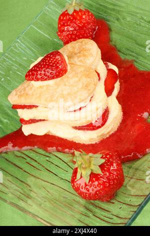 Fraises en forme de coeur et millefeuille de crème anglaise sur une sauce fraise, sur un fond vert. Pour une douce Saint Valentin. Mise au point sélective Banque D'Images