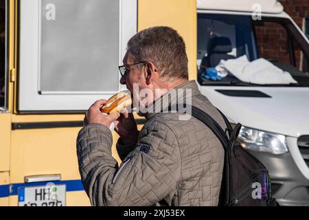 Homme mangeant fischbrötchen ou burger de poisson au marché du dimanche Fischmarkt dans le quartier Altona de Hambourg, Allemagne Banque D'Images