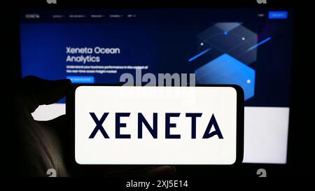 Stuttgart, Allemagne, 02-13-2024 : personne tenant un téléphone portable avec le logo de la société norvégienne d'analyse d'expédition Xeneta COMME en face de la page Web de l'entreprise. Banque D'Images