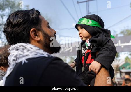 Un père tient son enfant vêtu de vêtements religieux dans ses bras lors d'une procession le neuvième jour de Mouharram. Le 9 de Muharram, les eaux sereines de Srinagar assistent à une procession unique et poignante de muharram tandis que les dévots à bord des bateaux rendent hommage, mêlant tradition et beauté tranquille du lac Dal. Mouharram est le premier mois du calendrier islamique, et l'un des mois les plus saints de l'Islam. Les musulmans chiites commémorent Mouharram comme un mois de deuil en souvenir du martyre de l'imam Hussain, le petit-fils du prophète Mahomet. L'imam Hussain a été martyrisé à Ashura, le 10ème jour de Mu Banque D'Images