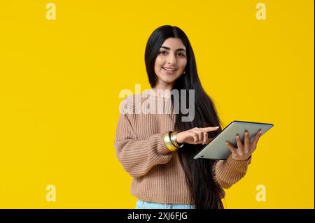 Belle jeune femme indienne heureuse avec tablette sur fond jaune Banque D'Images