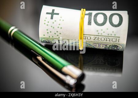 Une image en gros plan montrant une note de zlotys polonais roulée de 100 fixée avec une bande de caoutchouc jaune, aux côtés d'un stylo vert sophistiqué, mettant en évidence les thèmes L. Banque D'Images