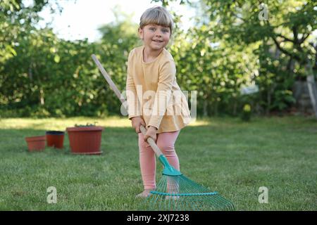 Mignonne petite fille avec râteau dans le jardin le jour de printemps Banque D'Images