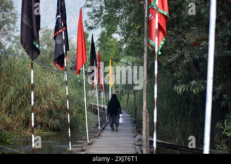 Srinagar, Inde. 16 juillet 2024. Srinagar, Cachemire, Inde, le 16 juillet 2024 : le 9 Muharram, des femmes musulmanes chiites traversent une passerelle en bois décorée de drapeaux dans les intérieurs pittoresques du lac Dal, à Srinagar. La pratique de la 9ème procession de Muharram sur Shikaras dans le lac Dal, Srinagar, remonte à l'ère Dogra. Cette tradition vénérée fait partie intégrante de la culture cachemirienne, célébrant Mouharram et rendant hommage au martyre de l'imam Hussain. Photo danoise Showkat/Sipa USA. Crédit : Sipa USA/Alamy Live News Banque D'Images