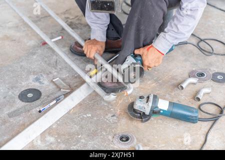 Le travailleur utilise des tuyaux en acier inoxydable coupés par meulage électrique à l'aide d'une meuleuse d'angle pour souder davantage dans un atelier de fer. Banque D'Images