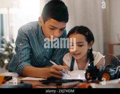 Enfants, frères et sœurs et écriture avec livre pour la robotique, projet scientifique ou art et artisanat à la maison. Enfants ou frère enseignant soeur avec cahier pour Banque D'Images