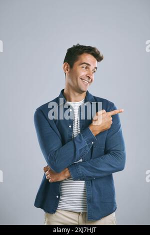 Portrait, pointage et homme avec revue, promotion et modèle sur fond gris de studio. Visage, personne et gars avec geste de la main, espace maquette ou Banque D'Images