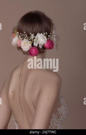 Une femme aux longs cheveux bruns ornés d'une couronne de fleurs pose pour un portrait. Elle porte une dentelle, robe perlée et son dos est tourné vers Banque D'Images