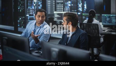 Jeunes collègues travaillant sur des ordinateurs et ayant une conversation sur un lieu de travail. Deux développeurs de logiciels indiens discutent d'une solution pour leur projet collaboratif d'intelligence artificielle Banque D'Images
