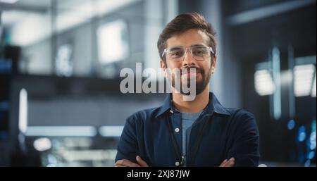 Beau Indien portant des lunettes et une chemise bleu foncé souriant et regardant la caméra. Jeune homme d'Asie du Sud travaillant comme ingénieur ou scientifique dans l'installation de recherche technologique Banque D'Images