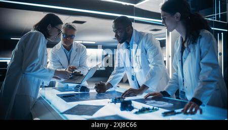 Équipe diversifiée de spécialistes en robotique industrielle travaillant sur des mains prothétiques innovantes dans des installations de recherche. Jeunes ingénieurs discutant du prototype, testant les composants électroniques. Banque D'Images