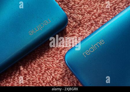 Terengganu, Malaisie - 2 août 2024 : gros plan du logo realme sur le panneau arrière du smartphone sur fond rouge. Smartphone realme bleu. Banque D'Images