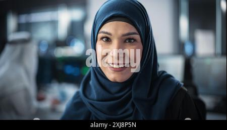 Portrait d'une jeune femme arabe habilitée dans le Hijab regardant caméra et souriant charmante. Spécialiste du moyen-Orient au travail, responsable des technologies de l'information, professionnel du génie logiciel Banque D'Images