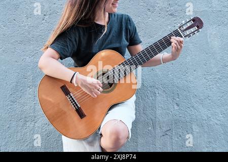photographie d'une femme méconnaissable jouant de la guitare acoustique sur un fond neutre Banque D'Images