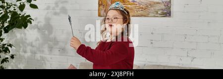 Une petite fille atteinte du syndrome de Down joue avec une baguette tout en portant une couronne. Banque D'Images