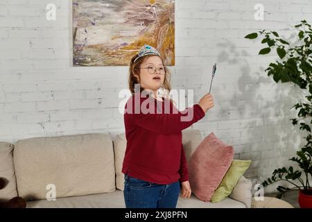 Une petite fille atteinte du syndrome de Down joue avec une baguette tout en portant une couronne. Banque D'Images