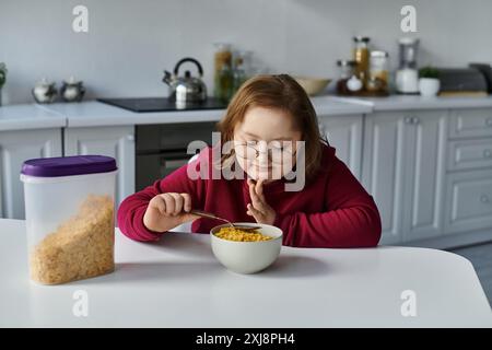 Une petite fille atteinte du syndrome de Down aime un bol de céréales à la maison. Banque D'Images