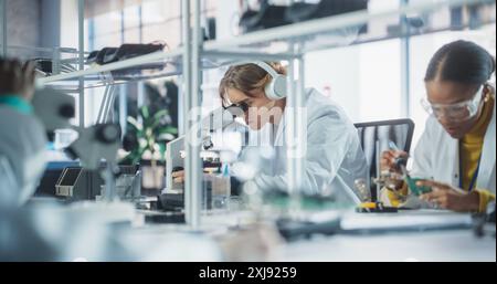 Équipe d'étudiants en sciences multiethniques menant des expériences électroniques dans un atelier universitaire. Divers jeunes camarades de classe utilisant des microscopes, travaillant avec le fer à souder pour créer une carte de circuit imprimé Banque D'Images