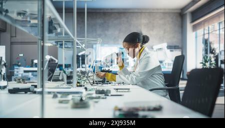 College Science Classroom : Groupe multiethnique diversifié d'étudiants expérimentant avec des composants informatiques, des cartes de circuit à souder, en utilisant des microscopes. Enseignant marchant et observant l'expérience Banque D'Images