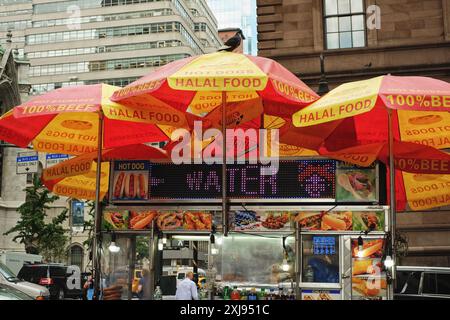 Un food truck à emporter au large de la Cinquième Avenue à New York avec des parapluies rouges et jaunes faisant la publicité de Halal Food, Hot Dog, 100% bœuf, nourriture et foi Banque D'Images