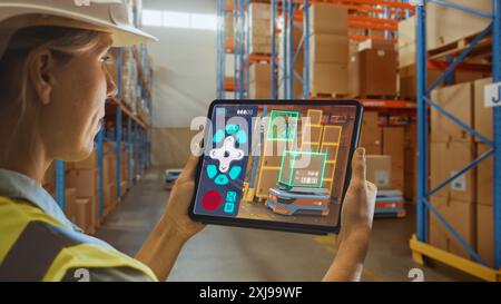 Concept de technologie future : femme ouvrière tenant tablette avec application de télécommande AR pour robot AGV d'entrepôt de détail avec infographie. Femmes contrôlant des véhicules guidés automatisés avec des forfaits. Banque D'Images