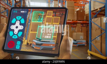 Concept de technologie future : travailleur tenant tablette avec application AR de télécommande pour robot AGV d'entrepôt de détail automatisé avec infographie. Véhicules guidés automatisés livrant des marchandises et des produits. Banque D'Images