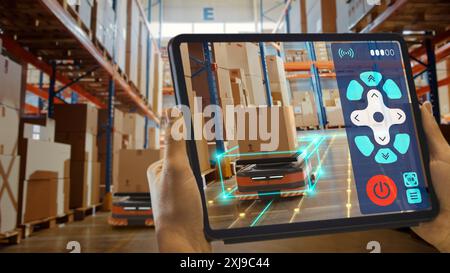 Concept de technologie future : travailleur tenant tablette avec application AR de télécommande pour robot AGV d'entrepôt de détail automatisé avec infographie. Véhicules guidés automatisés livrant des marchandises, des produits. Banque D'Images