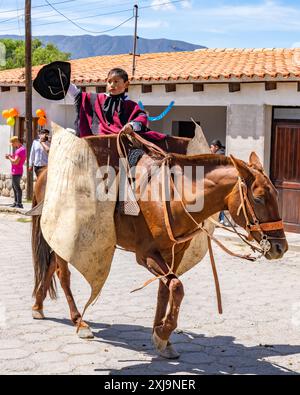 Un jeune gaucho dans un poncho traditionnel rouge Salteño agite son sombrero dans un défilé à Cachi, en Argentine. Les guardamontes en cuir de vache protègent le cavalier contre Banque D'Images