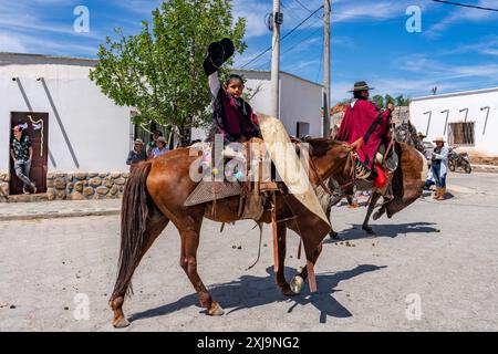 Un jeune gaucho dans un poncho traditionnel rouge Salteño agite son sombrero dans un défilé à Cachi, en Argentine. Les guardamontes en cuir de vache protègent le cavalier contre Banque D'Images