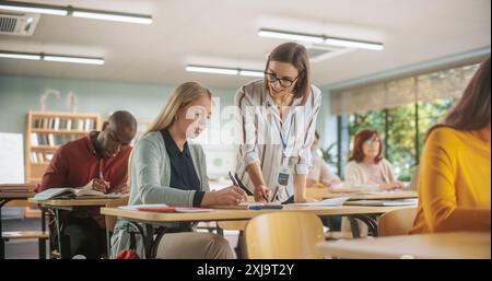 Jeune enseignant utile parlant avec une femme d'âge moyen, aidant à trouver une solution pour un exercice de cours d'examen. Femmes et hommes multiethniques d'âge différent acquérir de nouvelles compétences académiques en classe Banque D'Images