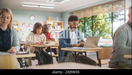 Groupe d'étudiants internationaux matures étudiant en classe. Centre de formation moderne pour adultes aider les gens à développer de nouvelles compétences utiles tout au long de la vie. Adultes écrivant dans des cahiers et utilisant des ordinateurs Banque D'Images