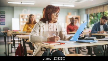 Hommes et femmes adultes acquérir des connaissances spécialisées sur un cours du soir au collège. Femme senior écrivant des notes dans le carnet de notes. Enseignant marchant entre les bureaux et donnant une conférence Banque D'Images