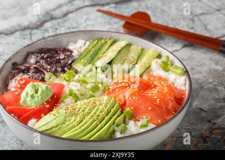 Bol à sushi maison avec saumon, riz blanc, légumes, algues, gingembre mariné et wasabi gros plan sur la table. Horizontal Banque D'Images