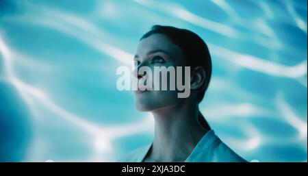 Séance de beauté captivante : jeune modèle féminin en manteau blanc minimaliste debout dans une pièce abstraite fond d'eau. Fille pose avec un sens de poise et Cyberpunk style Banque D'Images