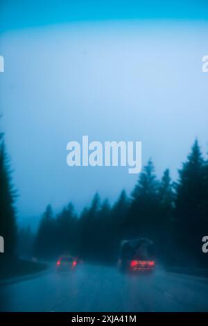 Voitures et camions conduisant sous de fortes pluies sur une route à travers une forêt, Snoqualmie Pass, WA, États-Unis Banque D'Images