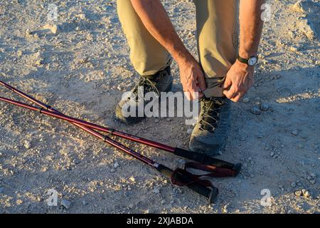 Concept de randonnée un homme attache ses lacets de bottes de randonnée. Des bâtons de randonnée sont au sol Banque D'Images