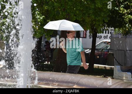 Une vague de chaleur prolongée approche du pic à Athènes Un homme tient un parapluie pour se protéger en passant devant une fontaine sur la place Syntagma alors qu'une vague de chaleur prolongée approche du pic à Athènes. Athènes Grèce Copyright : xNicolasxKoutsokostasxNicolasxKoutsokostasx DSC 202407170174 Banque D'Images