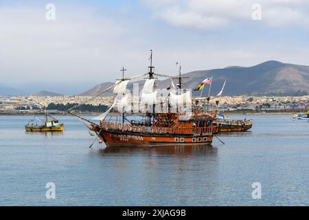 Coquimbo, Chili - 15 mars 2019 : un navire de style vintage ancré dans une baie calme avec un paysage urbain et des montagnes en arrière-plan. Banque D'Images