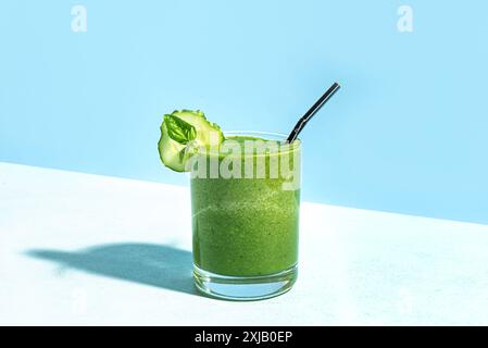 Smoothie vert en verre avec tranche de concombre et basilic sur fond bleu clair, tir à la mode avec une lumière dure. Modèle de concept publicitaire créatif de Banque D'Images