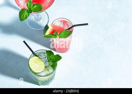 Cocktails d'été à la mode avec pastèque, citron vert, menthe et glace sur fond bleu, vue de dessus, espace de copie. Cocktail d'été, concept de bar de plage. Banque D'Images