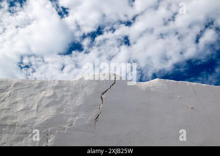 Vieux mur blanc d'une clôture avec une grosse fissure. Ciel bleu avec des nuages blancs intenses en arrière-plan. Caleta del Sebo, la Graciosa, Îles Canaries, Espagne. Banque D'Images