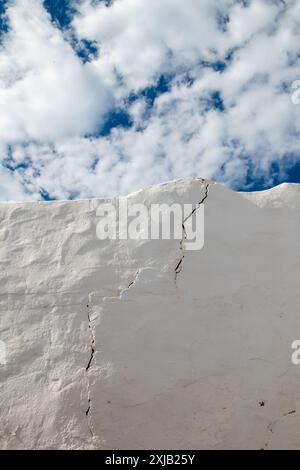 Vieux mur blanc d'une clôture avec une grosse fissure. Ciel bleu avec des nuages blancs intenses en arrière-plan. Caleta del Sebo, la Graciosa, Îles Canaries, Espagne. Banque D'Images