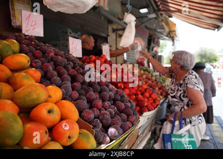 Une dame âgée portant des vêtements d'été obtient d'un vendeur un sac avec des nectarines qu'elle a acheté, Machane Yehuda marché stand avec aussi de la mangue, des prunes et des pêches Banque D'Images