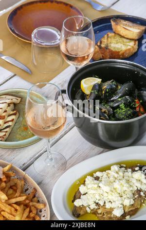 Jeune femme enjoigniyng dîner dans le restaurant méditerranéen. Verre de rose et divers plats servis sur la table. Banque D'Images