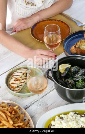 Jeune femme enjoigniyng dîner dans le restaurant méditerranéen. Verre de rose et divers plats servis sur la table. Banque D'Images